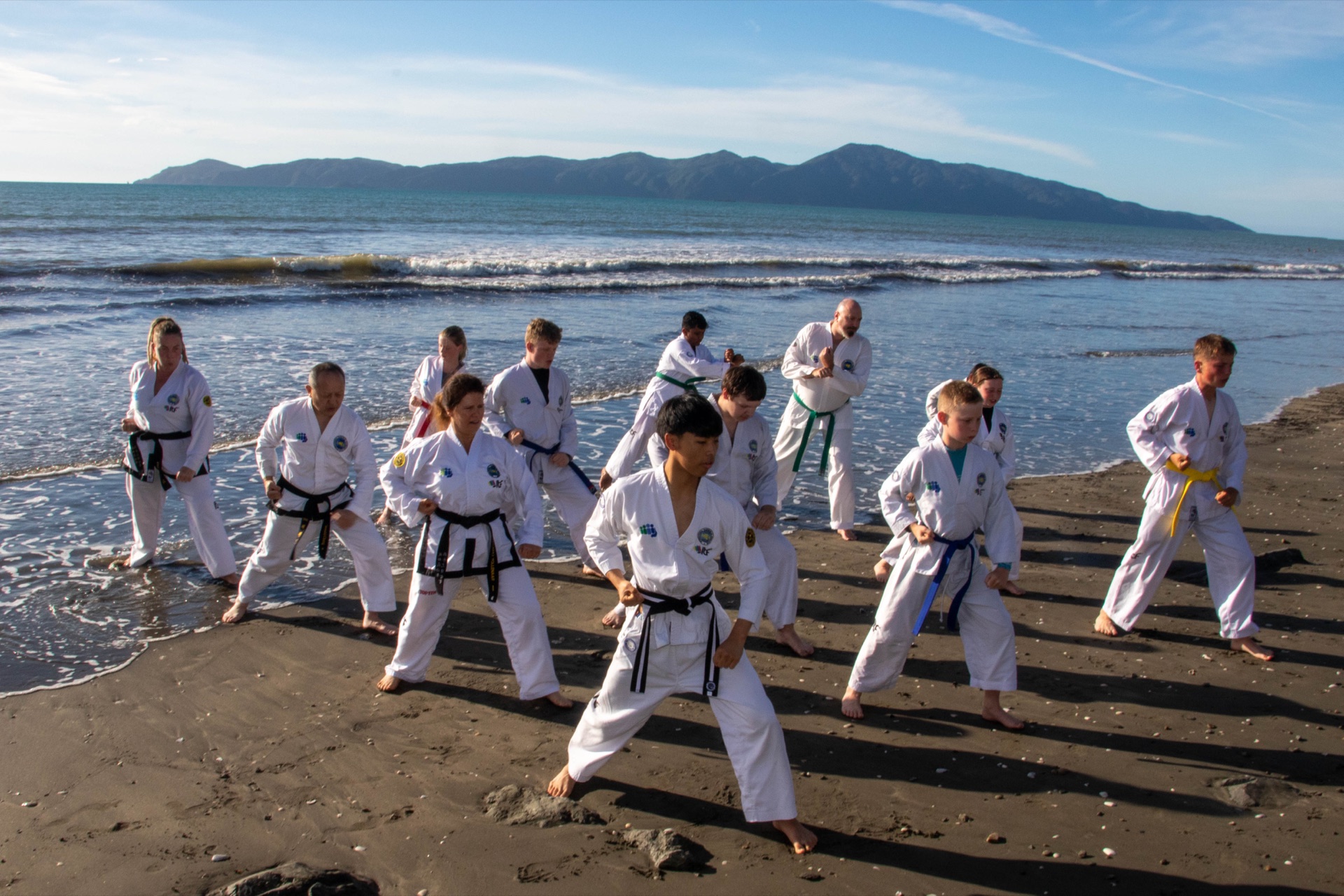 Kāpiti Coast TaeKwon-Do Club members of all ages training together on the beach, Kāpiti Island in the background
